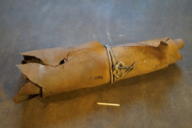 Ein brauner Papiertüte, die wie eine Granate aussieht, mit einem Seil verschnürt und auf einem Tisch platziert, mit einer Zigarette daneben.