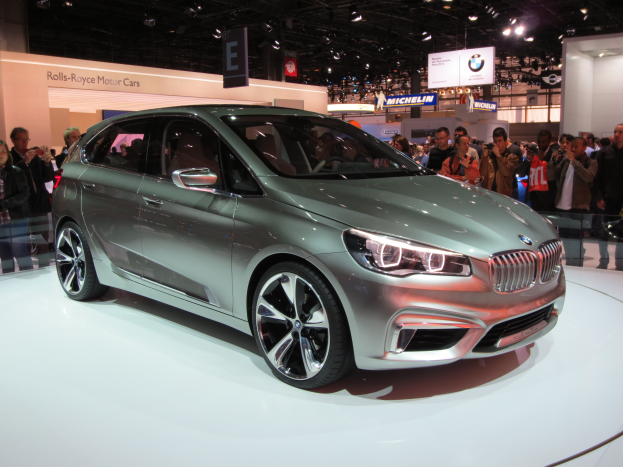 Ein BMW 2er Active Tourer Concept auf der IAA in Frankfurt, umgeben von Menschen, die Fotos machen, mit beleuchteten Schildern im Hintergrund.