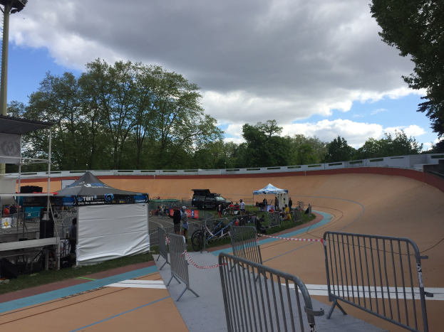 Gruppe von Radfahrern auf einer Schotter-BMX-Strecke bei den 2018 UCI BMX-Weltmeisterschaften, mit Zelten, Fahrzeugen und Bäumen im Hintergrund.