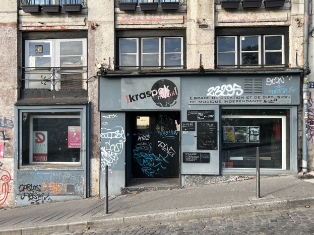 Gebäude mit Fenstern, Geländern, Türen, Texttafeln, Plakaten, Pfählen und Graffiti an seiner Seite, das über einer Straße liegt.