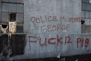 Ein Gebäude mit Graffiti, das "Polizei ermordet George Fuck 12 P19" auf der Seite trägt, mit Fenstern und verschiedenen Gegenständen davor.