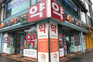 Ein Gebäude mit Glaswänden und -türen, auf denen Schilder mit der Aufschrift "Südkoreas erste Apotheke in Seoul, Südkorea" und ein Schild an der Seite zu sehen sind.