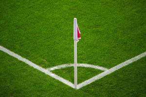 Ein Fuballfeld mit grünem Gras, weißen Begrenzungslinien und einem weißen Pfahl mit einer roten und weißen Flagge, die den Elfmeterpunkt in der Mitte markiert.