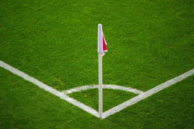 Ein Fuballfeld mit grünem Gras, weißen Begrenzungslinien und einem weißen Pfahl mit einer roten und weißen Flagge, die den Elfmeterpunkt in der Mitte markiert.