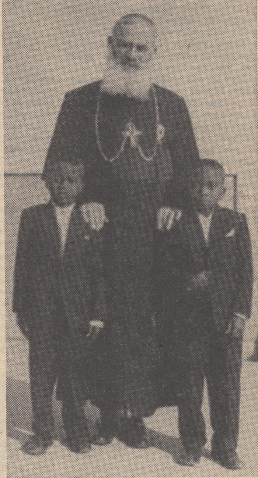 Ein Schwarz-Weiß-Foto eines Mannes, der neben zwei Jungen in Blazern und Krawatten steht, mit Text unten, der ihn als ihren Vater identifiziert.