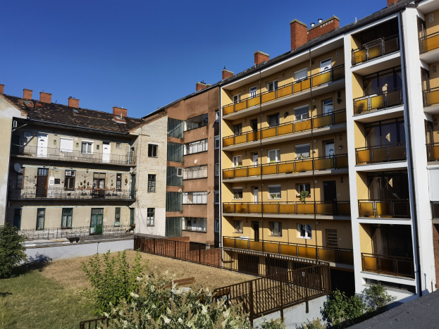 Wohngebäude mit Innenhof, der mit grünem Gras, Pflanzen, Bäumen, Fenstern, Türen, Geländern und einem sichtbaren Himmel im Hintergrund ausgestattet ist.