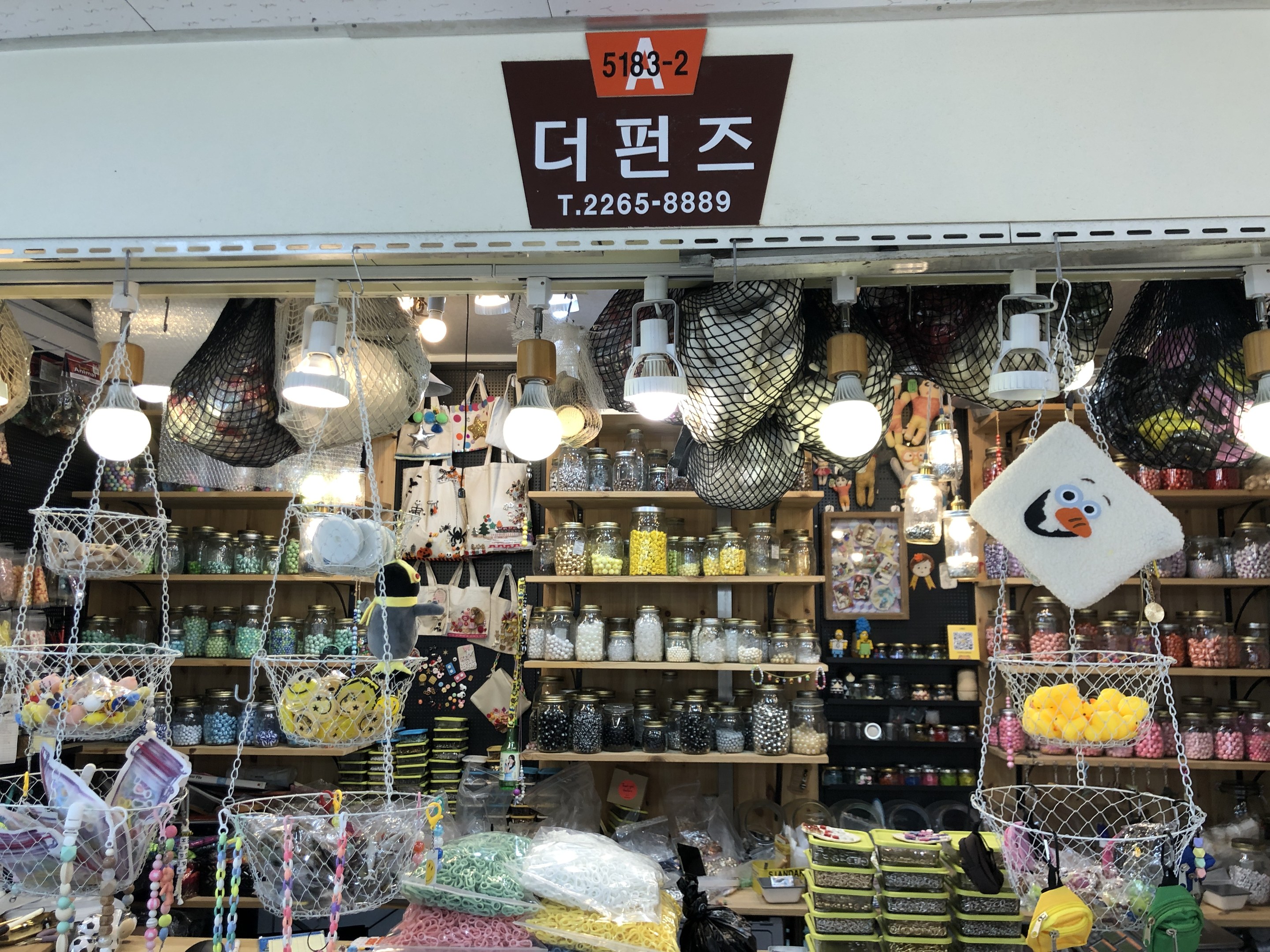 Ein unordentlicher Laden in Seoul mit verschiedenen Artikeln wie Körben, Lampen, Flaschen und Spielzeugen auf Regalen, mit einer Tafel oben, die ihn als einen der besten koreanischen Läden ausweist.