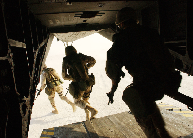 Soldaten in Uniform und Helmen steigen aus einem Flugzeug aus und halten Gewehre, was auf einen Militäreinsatz hinweist.