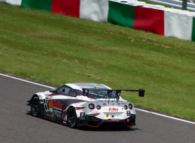Ein Nissan GT-R Nismo GT3 Rennwagen auf der Nürburgring 24 Stunden Strecke, mit grünem Gras und einer Absperrung im Hintergrund.