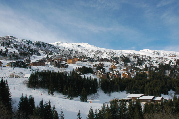 Picturesque view of a ski resort in the French Alps with snow-covered mountains, trees, buildings, and a clear blue sky.