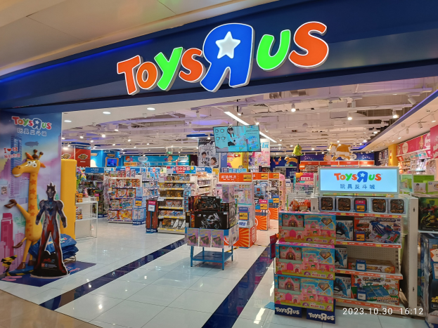 Ein Toys R Us Geschäft im Einkaufszentrum mit Regalen voller Spielzeug, einem sichtbaren Namensschild, Deckenbeleuchtung und einem Wasserzeichen in der rechten unteren Ecke.