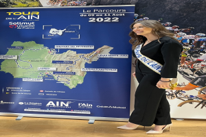 Eine Frau steht vor einer Fahne mit einer Karte von Frankreich, die ein Band trägt, auf dem "Tour de France 2020" steht.