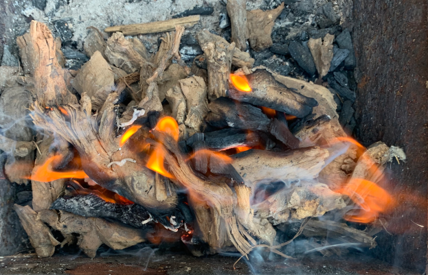 Ein Detailbild eines Kamins mit hell brennenden Holzscheiten, die in einem Haufen angeordnet sind, Flammen tanzen und flackern und Rauch aufsteigt.