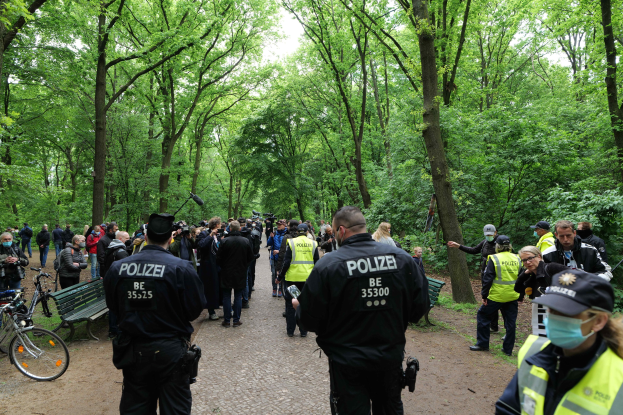 Gruppe von Polizisten vor einer Menge mit Fahrrädern und einer Bank im Vordergrund und Bäumen im Hintergrund.