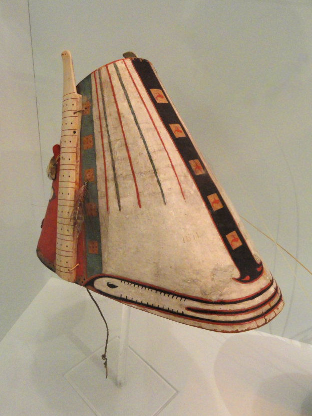 Eine hölzerne Balalaika in einer Glasvitrine auf einem weißen Untergrund mit einer Wand im Hintergrund.