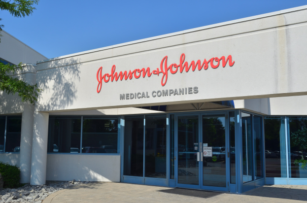 Außenansicht des Johnson & Johnson Medical Companies-Gebäudes mit Glaswänden, Text an der Fassade, Landschaftssteinen, Pflanzen und einem Baum unter einem klaren blauen Himmel.