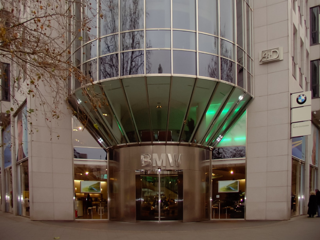 Großes BMW-Hauptquartier-Gebäude in Frankfurt, Deutschland, mit Glasfront, Text an der Fassade, Menschen vor dem Gebäude und einem Baum links.