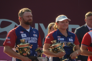 Eine Gruppe von Menschen, die nebeneinander stehen und jeweils einen Pokal halten, mit einem Schild im Hintergrund, auf dem 'World Archery Championships' steht.