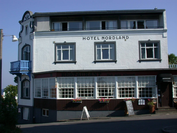 Hotel Nordland in Stavanger, Norwegen, mit einem Gebäude mit Fenstern, einem Schild, einem Straßenschild, Bäumen und einem bewölkten Himmel.