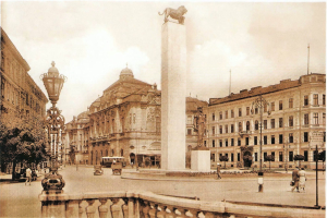 Ein altes Foto eines Stadtplatzes mit einer Statue in der Mitte, umgeben von Gebäuden, Straßenlaternen, Straßenlaternen, Kraftfahrzeugen auf der Straße, Menschen auf dem Gehweg, Bäumen und einem bewölkten Himmel im Hintergrund.