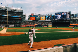 Baseballspiel im Gange im Yankee Stadium mit Spielern auf dem Feld und Zuschauern in den Rängen, umgeben von Stadionmerkmalen unter einem bewölktem Himmel.