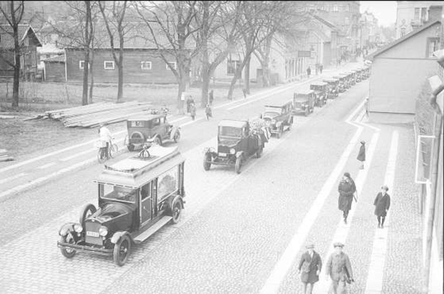 Schwarze und weiße Straßenszene in Berlin aus den 1930er-1940er Jahren, die Autos, Fußgänger, Gebäude mit Fenstern, Bäume und einen klaren Himmel zeigt.