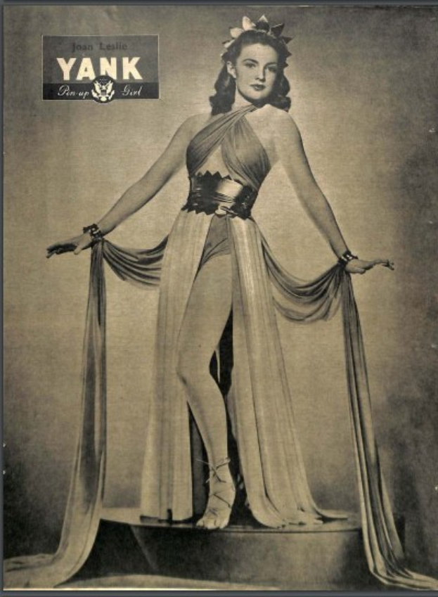 Ein Schwarz-Weiß-Porträt von Joan Leslie in einem langen, hochgeschlossenen Kleid mit langen Ärmeln, die selbstbewusst auf einer Bühne steht, eingerahmt von einem Photo-Rahmen und mit der Aufschrift "Joan Leslie" oben.