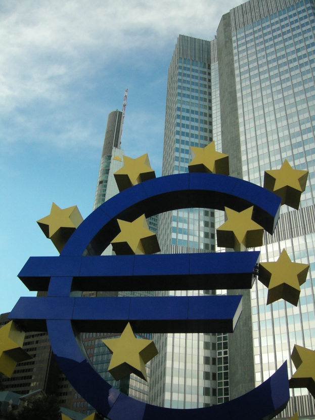 Das Euro-Zeichen vor dem Hauptquartier der Europäischen Zentralbank in Frankfurt, Deutschland, mit dem Gebäude umgeben von Bäumen und einem bewölkten Himmel.