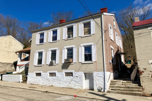 Eine Reihe von Häusern an einer Straßenecke mit verschiedenen architektonischen Details, Bäumen und Stromleitungen, unter einem bewölkten Himmel, zum Verkauf angeboten für $1.250.000.