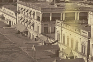 Schwarzes und weißes Foto einer Stadtstraße mit Gebäuden, die Fenster, Säulen, Namensschilder, Schuppen und Pfähle aufweisen.