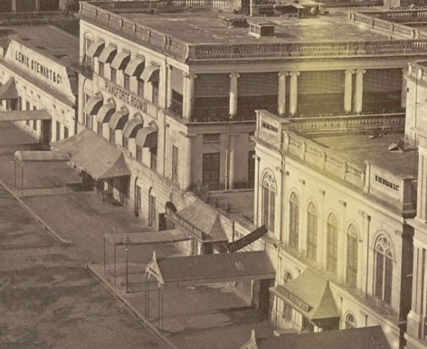 Schwarzes und weißes Foto einer Stadtstraße mit Gebäuden, die Fenster, Säulen, Namensschilder, Schuppen und Pfähle aufweisen.