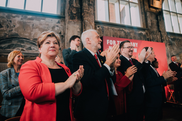 Eine Gruppe von Menschen, die jubelnd vor einer Menge stehen, mit einem Banner mit der Aufschrift "Wahlsieg" im Hintergrund.