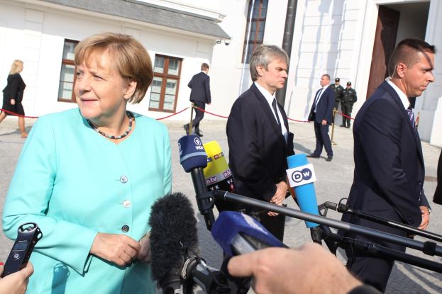 Bundeskanzlerin Angela Merkel bei einer Pressekonferenz im Kanzleramt in Berlin, umgeben von Menschen, einige mit Mikrofonen, mit Gebäuden im Hintergrund.
