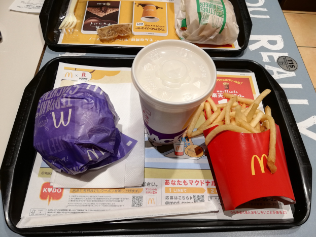 Ein Tisch mit einem Tablett, auf dem ein McDonald's-Essen mit Pommes, ein Kaffeebecher, ein Blatt Papier, eine Gabel und ein Messer liegt.