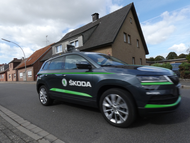 Schwarzer und grüner Skoda Kodiaq elektrischer SUV auf einer Stadtstraße mit Gebäuden, Bäumen und Laternen im Hintergrund.