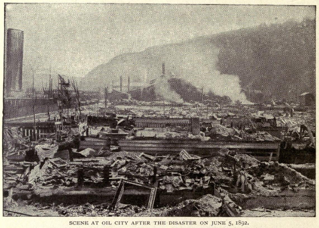 Schwarz-weiß-Foto einer Stadt nach einer Katastrophe am 5. Juni 1892, das beschädigte Gebäude, Masten, Rauch und einen Hügel im Hintergrund zeigt, mit Text unten.