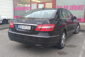 Schwarzer Mercedes-Benz E-Klasse E250 CDI BlueEfficiency Avantgarde auf einer Straße mit einem Gebäude mit Glastüren und Wandtext im Hintergrund.