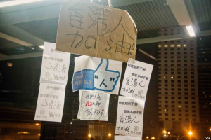 Menschen stehen vor einem beleuchteten Gebäude bei Nacht mit Schildern, die von der Decke hängen, wahrscheinlich protestieren sie gegen ein Social-Media-Verbot.