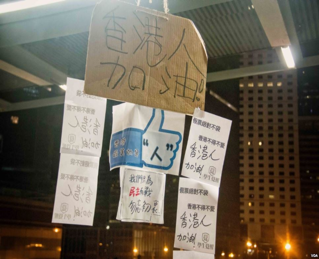 Menschen stehen vor einem beleuchteten Gebäude bei Nacht mit Schildern, die von der Decke hängen, wahrscheinlich protestieren sie gegen ein Social-Media-Verbot.