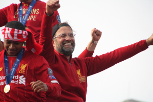 Liverpool-Trainer Jürgen Klopp feiert in rotem Jackett mit seinen medaillenbehangenen Spielern nach dem Gewinn der UEFA Champions League, mit dem Himmel im Hintergrund.