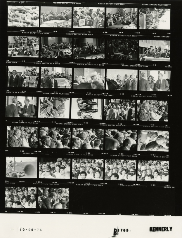 Schwarzes und weißes Foto einer vielseitigen Menge strahlender Menschen, die um einen Fernseher versammelt sind und in die Kamera schauen.