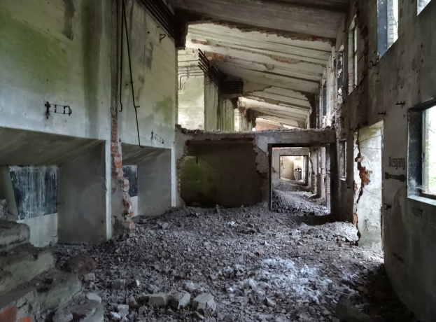 Altes Gebäude mit umfangreichen Trümmern, zerbrochenen Fenstern und verstreuten Trümmern, was auf schweren Verfall hinweist.