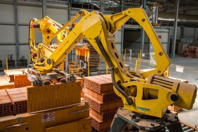 Großes industrielles Lagerhaus mit gestapelten Kisten, Kränen, Zaun, Strommasten und einer fernen Wand in einer automatisierten Fertigungsumgebung.