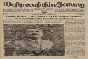 Adolf Hitler, in einem schwarzen Anzug und weißem Hemd, steht vor einer Menge auf der Titelseite einer deutschen Zeitung mit der Überschrift "Adolf Hitler - Der Erte Soldat Feines Volkes".