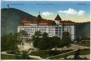 Eine alte Postkarte zeigt das Hotel Imperial in Karlsbad, Deutschland, ein großes Gebäude mit zahlreichen Fenstern, umgeben von Bäumen, Pflanzen und Gras, mit einem Weg, der zu ihm führt, vor einem Hintergrund von Hügeln unter einem bewölkten Himmel und Text oben auf dem Bild.
