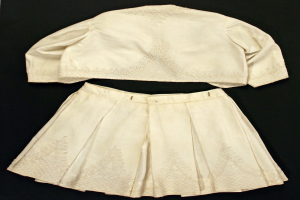 Ein weißer, geplusterter Rock mit hohem Bund und einem einfarbigen, weißen Kurzarmhemd mit rundem Halsausschnitt, beide auf einem schwarzen Hintergrund, das eine subtile Schimmer im Stoff zeigt.