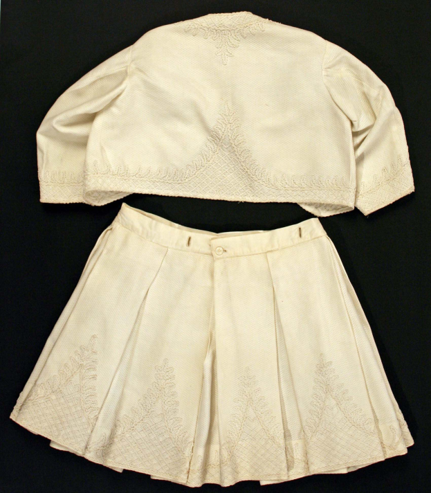 Ein weißer, geplusterter Rock mit hohem Bund und einem einfarbigen, weißen Kurzarmhemd mit rundem Halsausschnitt, beide auf einem schwarzen Hintergrund, das eine subtile Schimmer im Stoff zeigt.