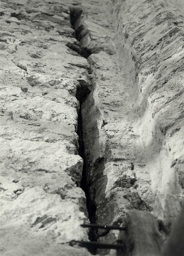 Schwarzes und weißes Foto eines großen Risses in einem Bodenkanal mit einem Wasserzeichen auf der linken Seite.