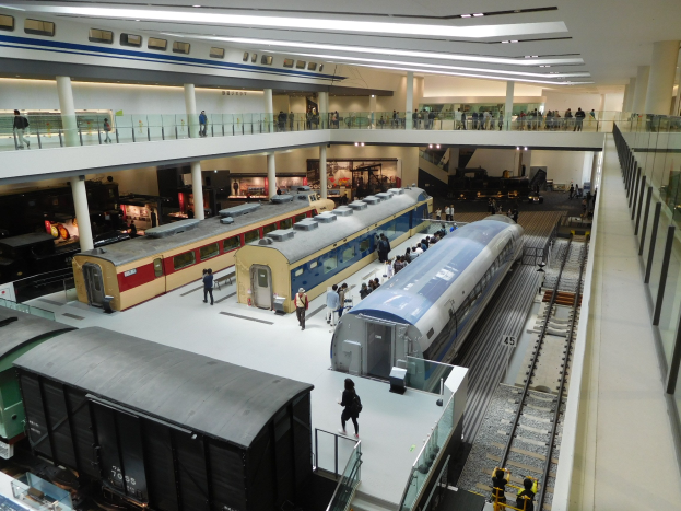 Ein großer Museumsraum mit verschiedenen Zügen in unterschiedlichen Gröüen und Farben, bei denen Menschen die Ausstellungsstücke betrachten.