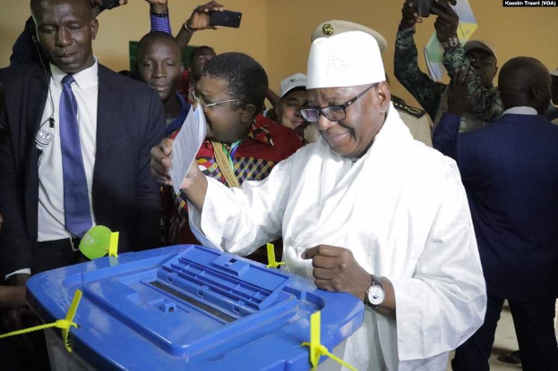 Ein Mann in einem weißen Anzug und Hut legt seine Stimme in eine blaue Wahlurne in einer Wahllokal in Abuja, Nigeria.
